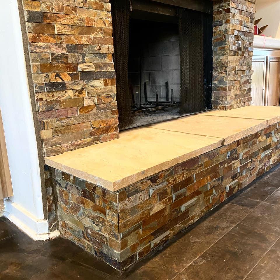 A stone fireplace with a wooden bench in front of it.