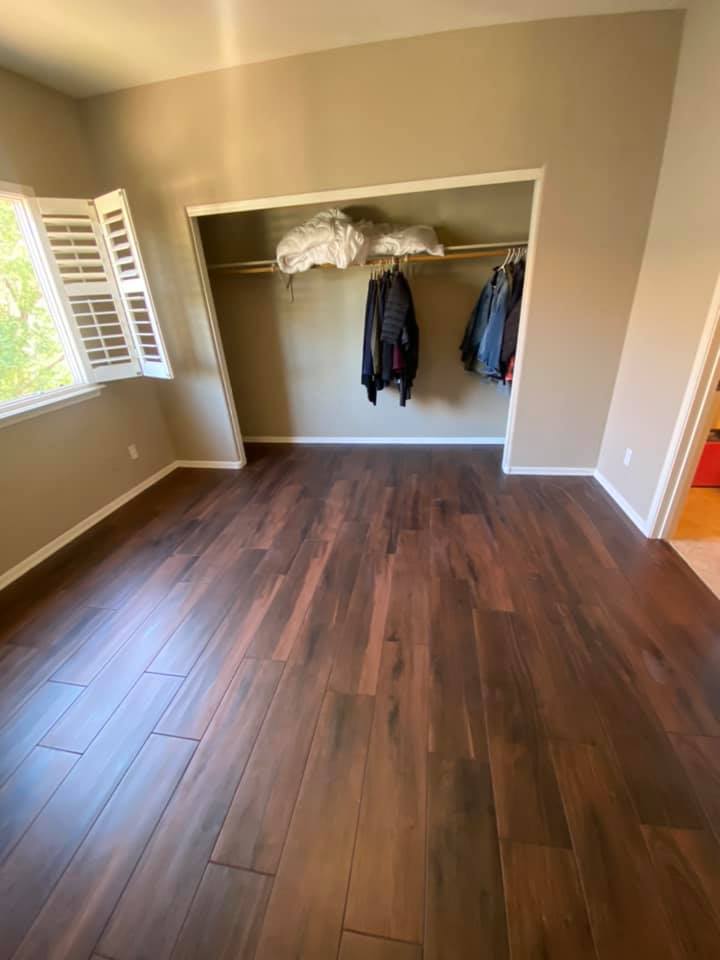 A bedroom with hardwood floors and a closet with clothes hanging on the racks.