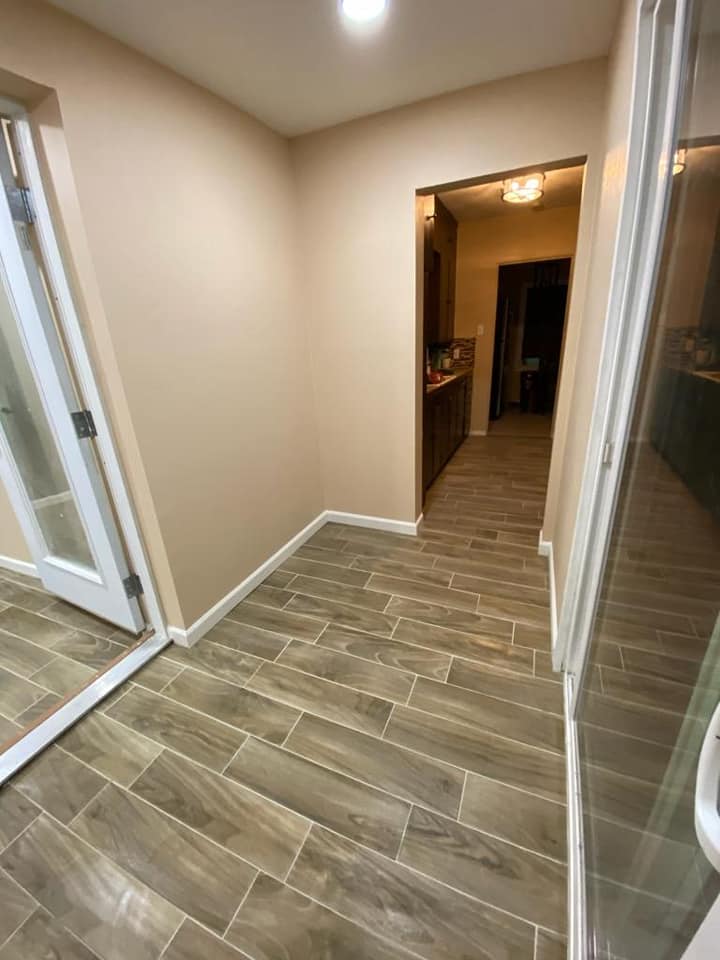 A hallway with a wooden floor and a glass door leading to a kitchen.