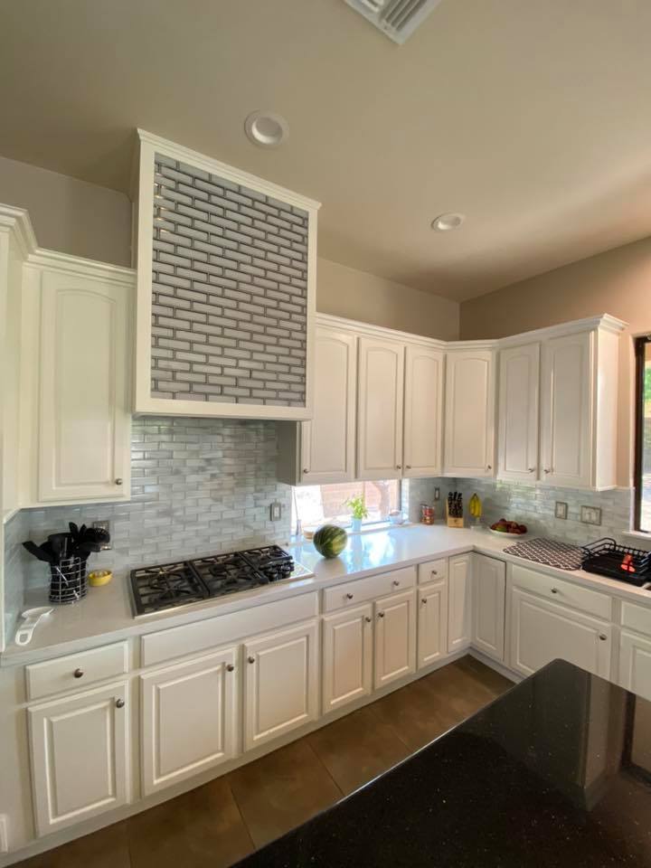 A kitchen with white cabinets , a stove , a sink and a hood.
