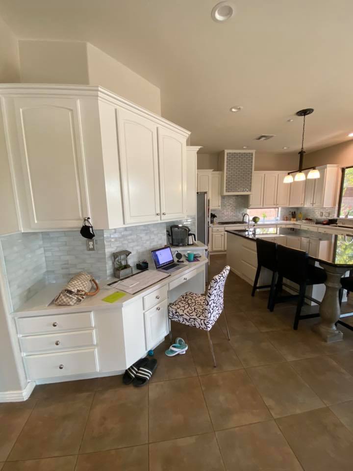 A kitchen with white cabinets and a desk with a laptop on it.