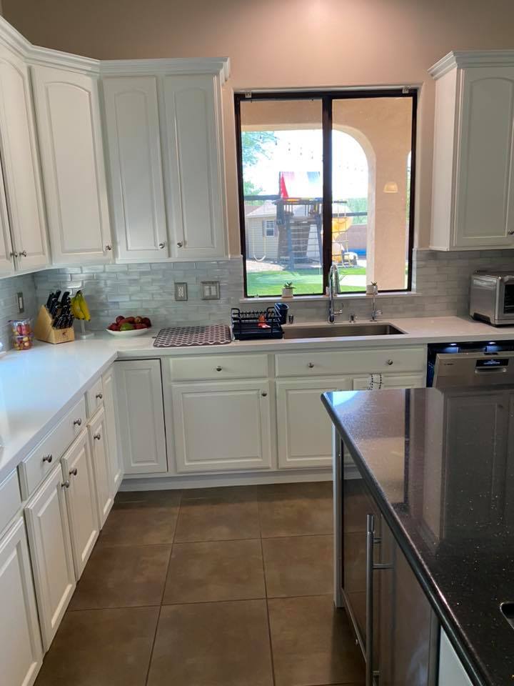 A kitchen with white cabinets , a sink , and a window.
