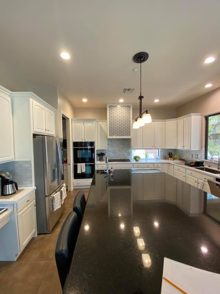 A kitchen with white cabinets , black counter tops , stainless steel appliances and a large island.