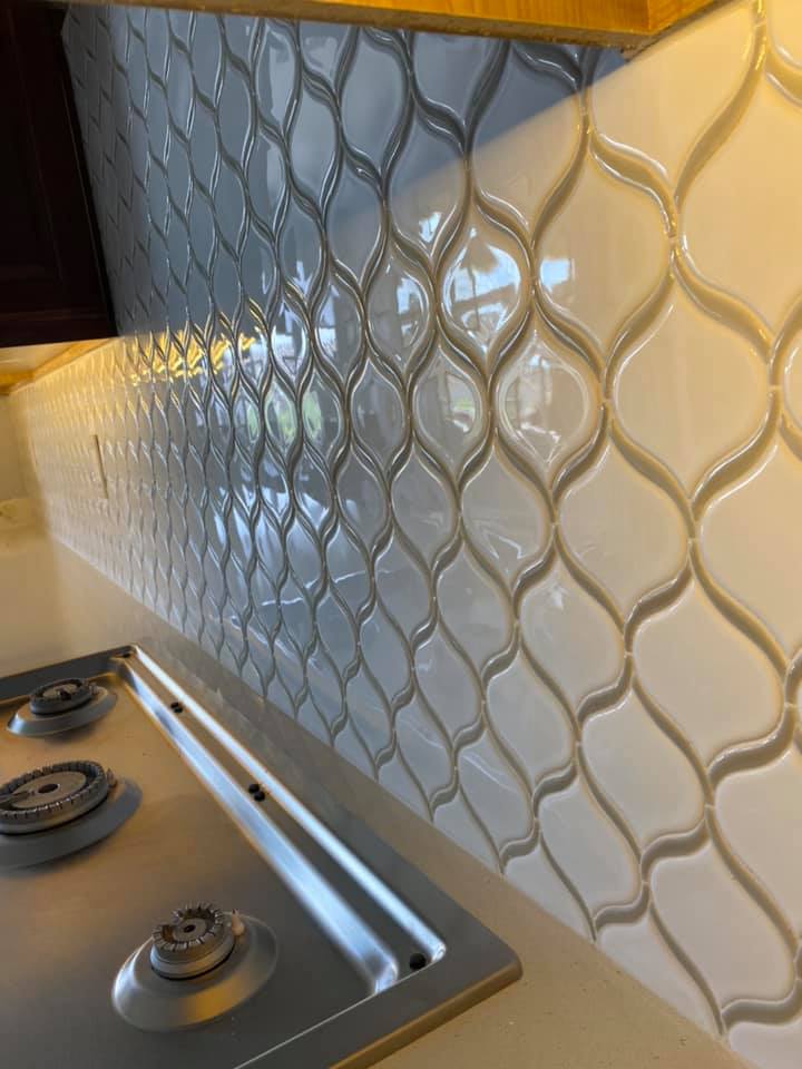 A kitchen with a stove top oven and white tiles on the wall.