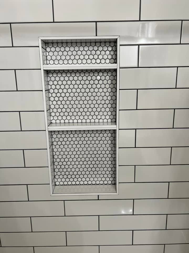 A shower niche in a bathroom with white tiles and a shelf.