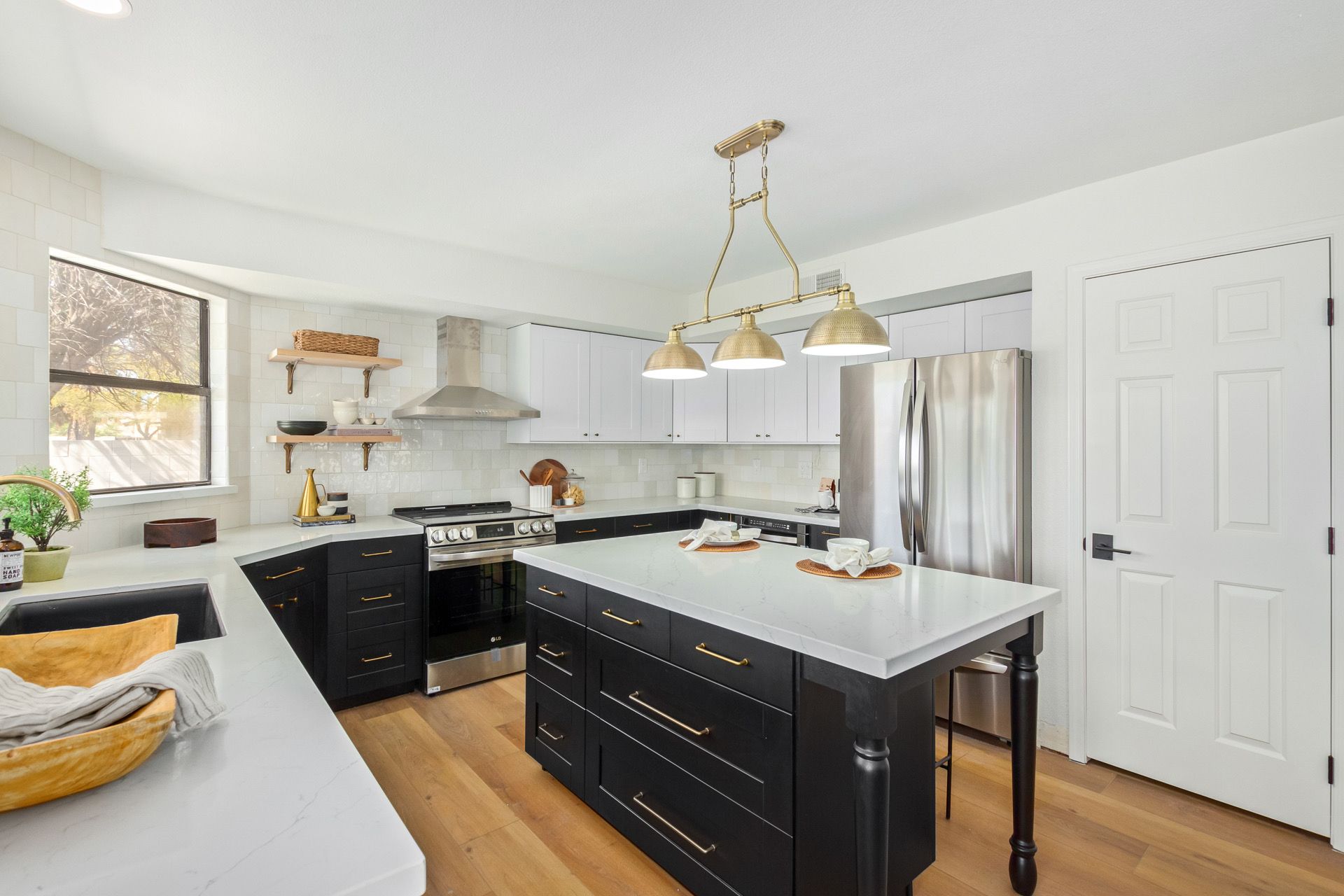 A kitchen with black cabinets , white counter tops , stainless steel appliances and a large island.