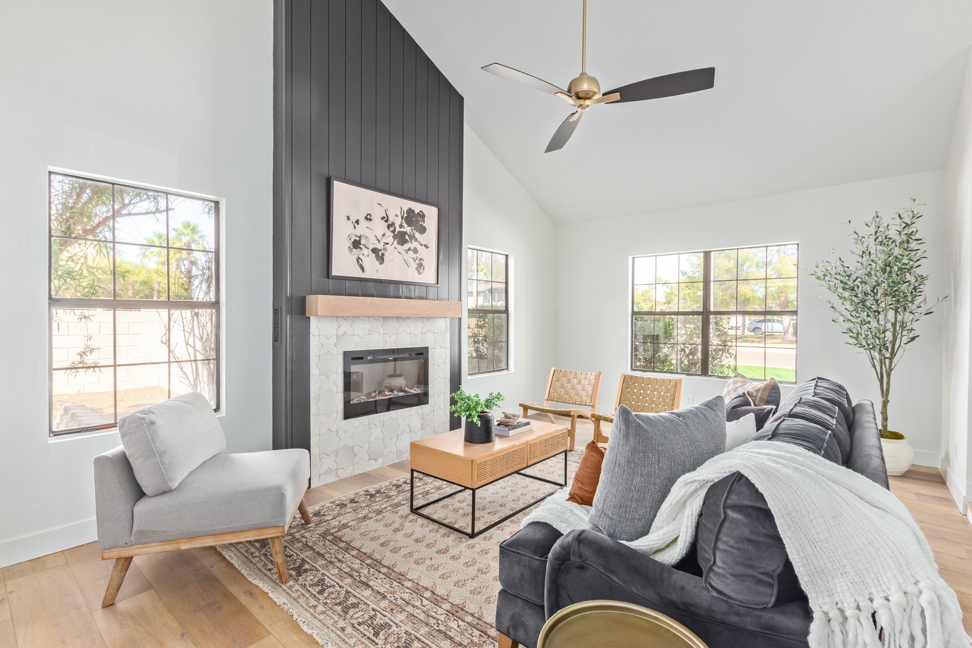 A living room with a couch , chair , coffee table , fireplace and ceiling fan.