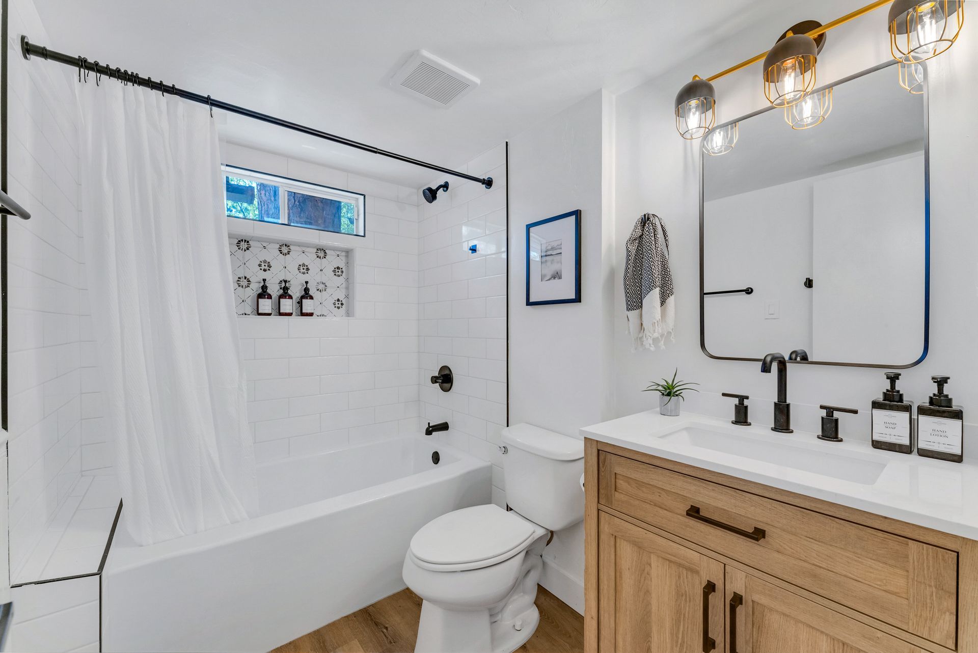 A bathroom with a toilet , sink , tub and mirror.