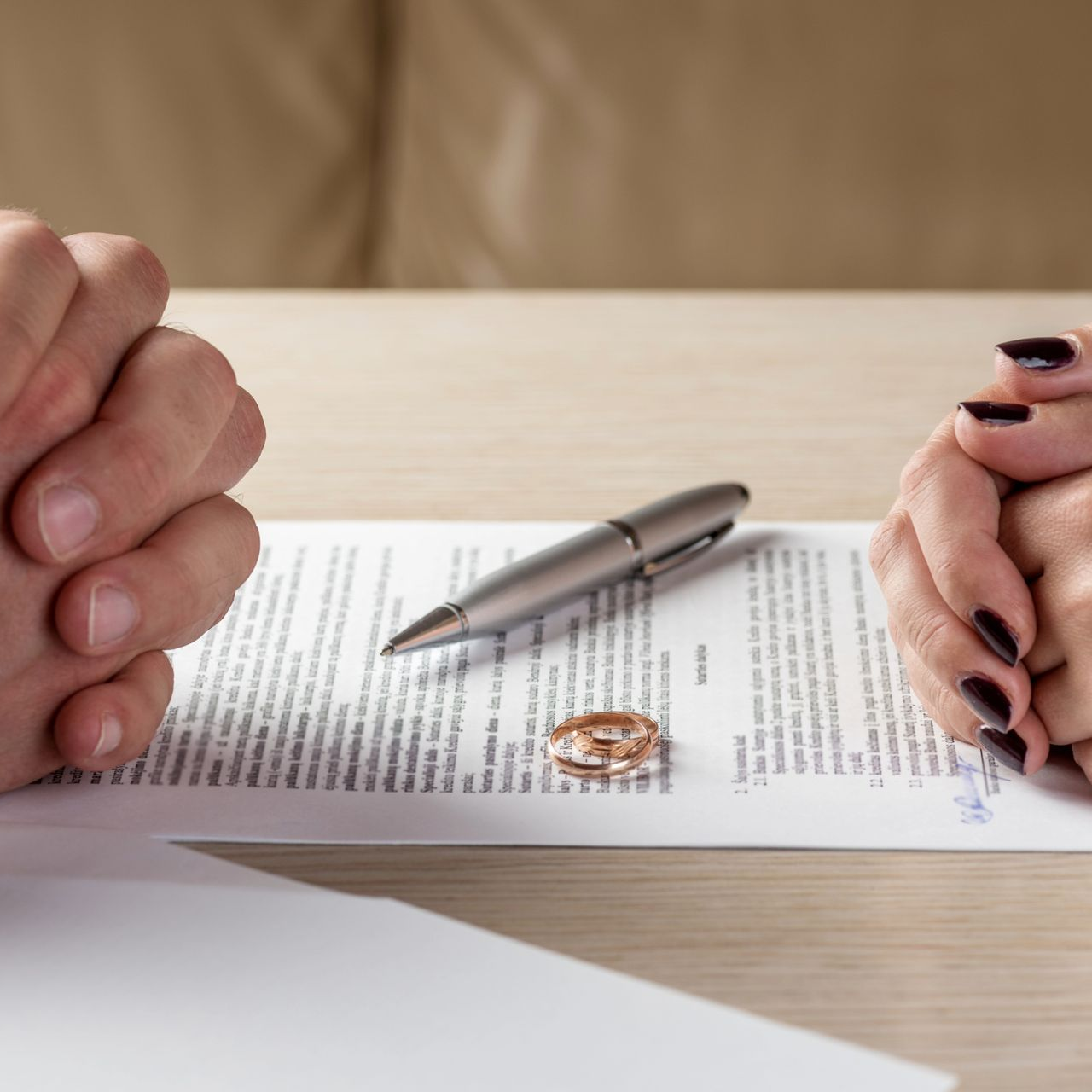 Hands flanking a divorce document, a wedding ring, and pen on a table.