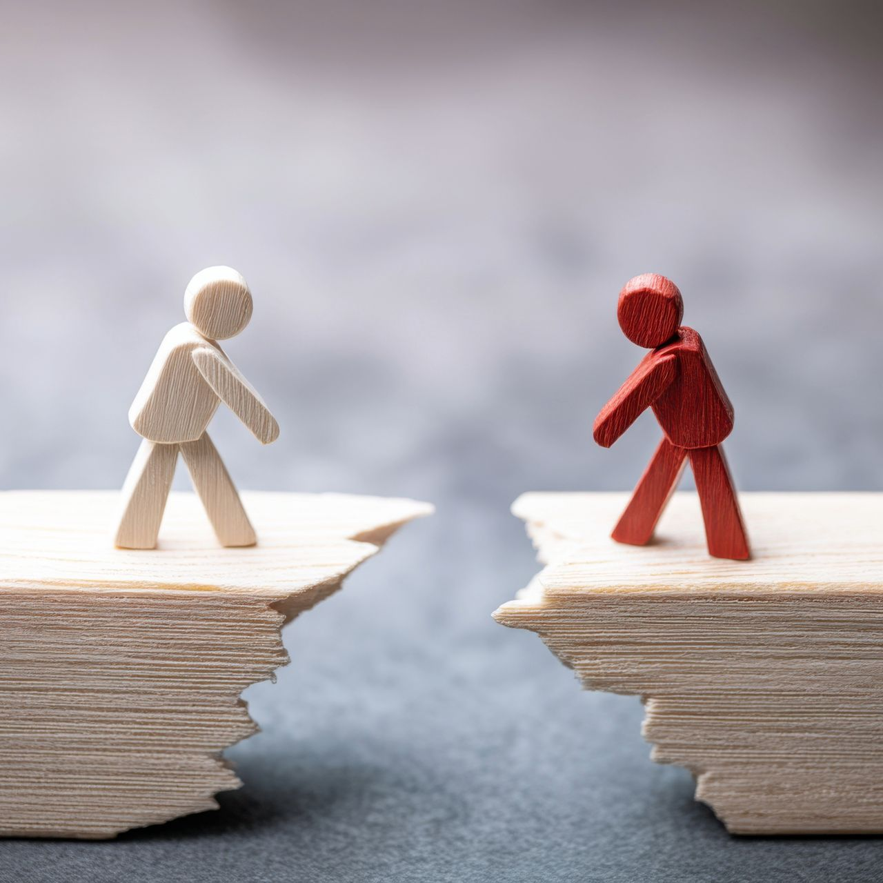 Wooden figures, one white, one red, facing each other across a gap, possibly representing a divide or challenge.