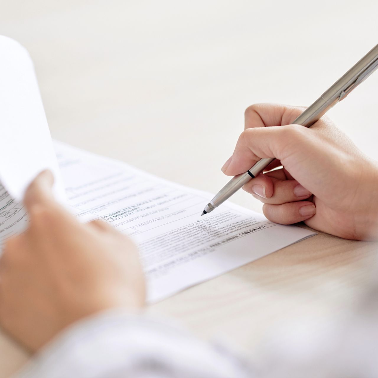 Person writing on a document with a pen, pages are white, light background.