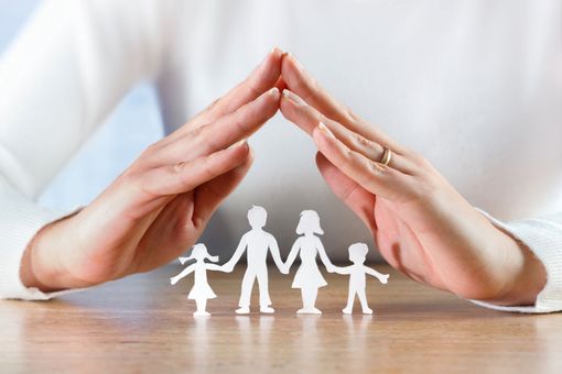 A hand forming a roof over a cut out of a family