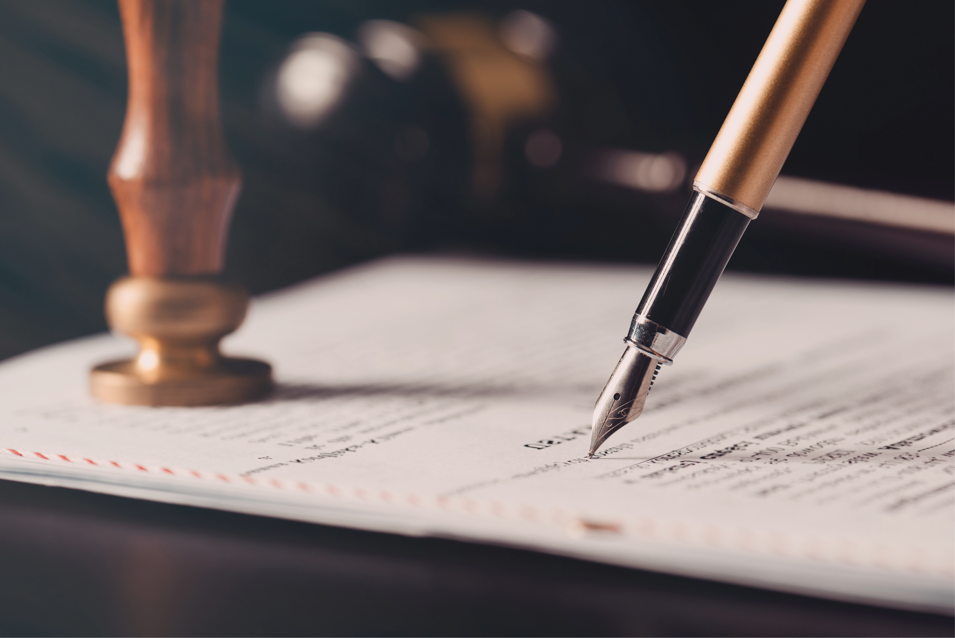 Fountain pen signing a legal document on a desk, with a stamp and gavel in the background.