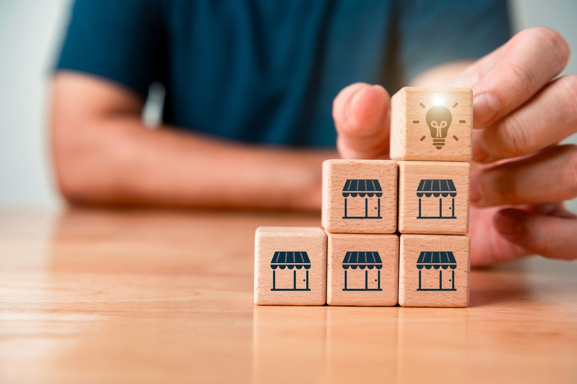 Hand stacking blocks, some with store icons, one with a lightbulb