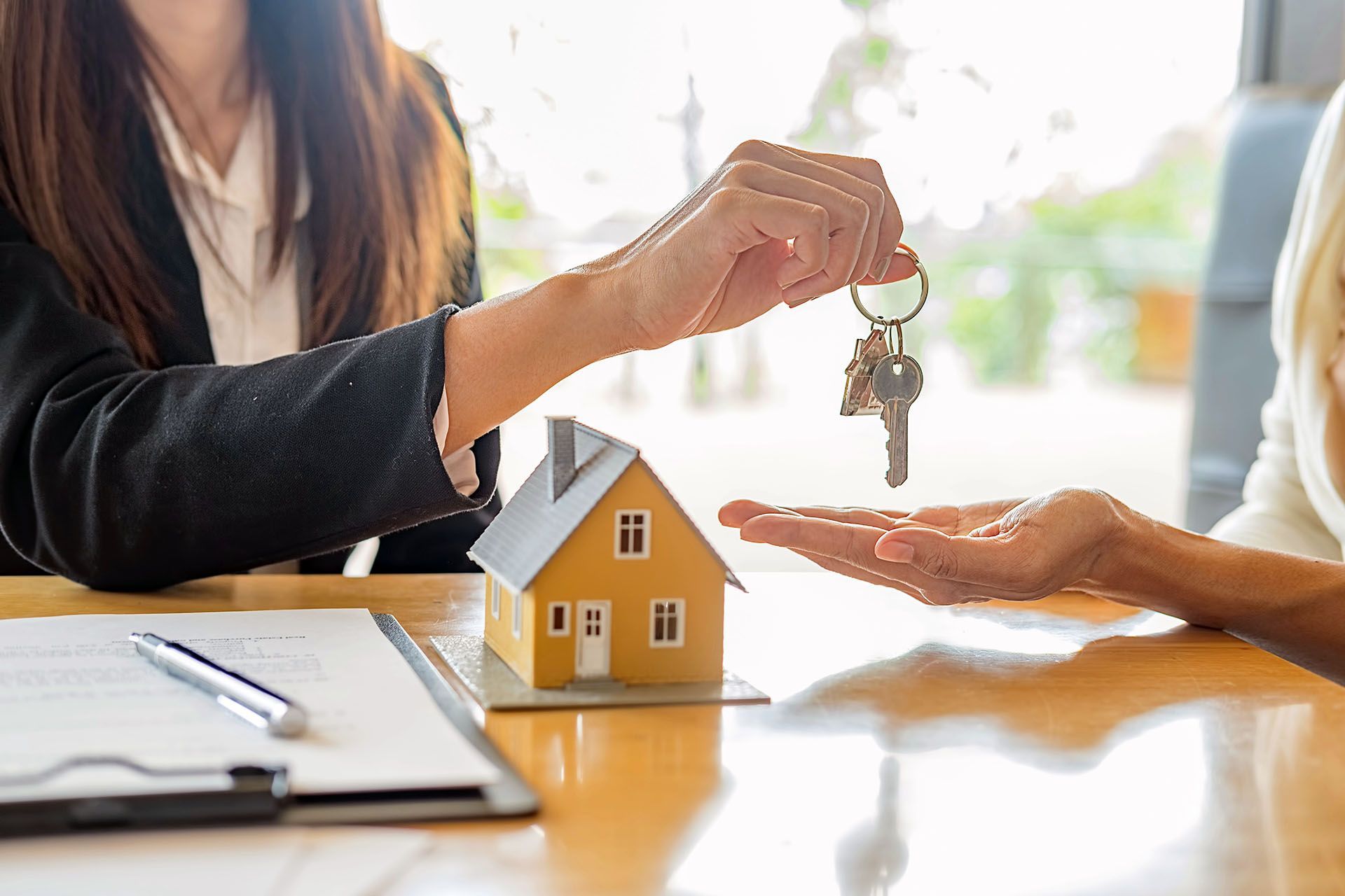 A woman is giving a key to another woman in front of a model house.