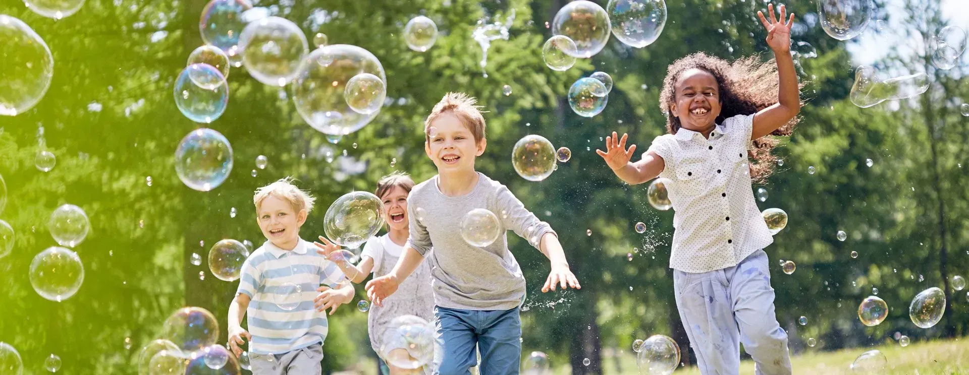 A group of children are running through soap bubbles in a park.