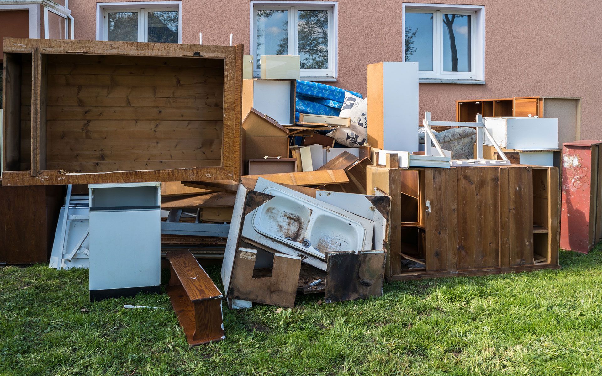A pile of junk is sitting in the grass in front of a building.