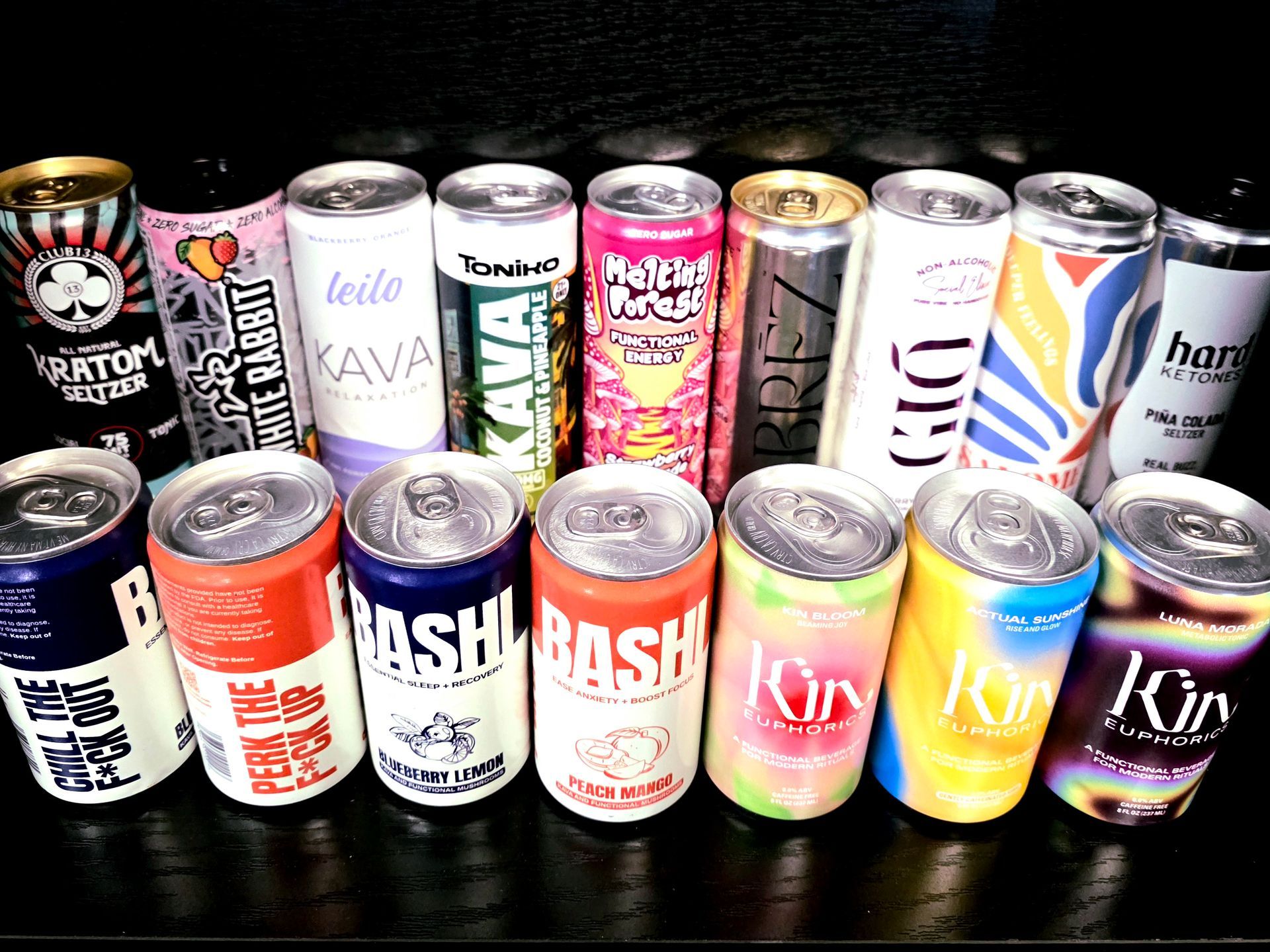 Rows of various canned functional beverages, including Kin Euphorics, Leilo, and other tonic drinks, arranged on a surface.