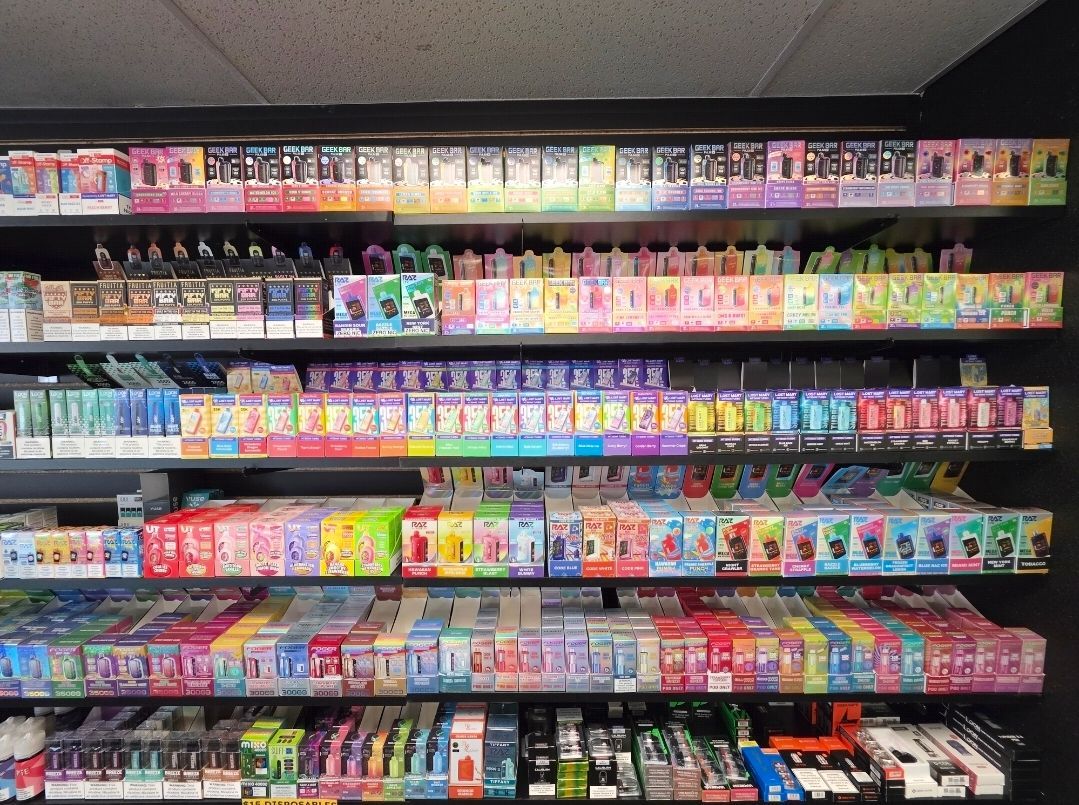 Shelves stocked with a large variety of colorful disposable vape product boxes in a retail display.