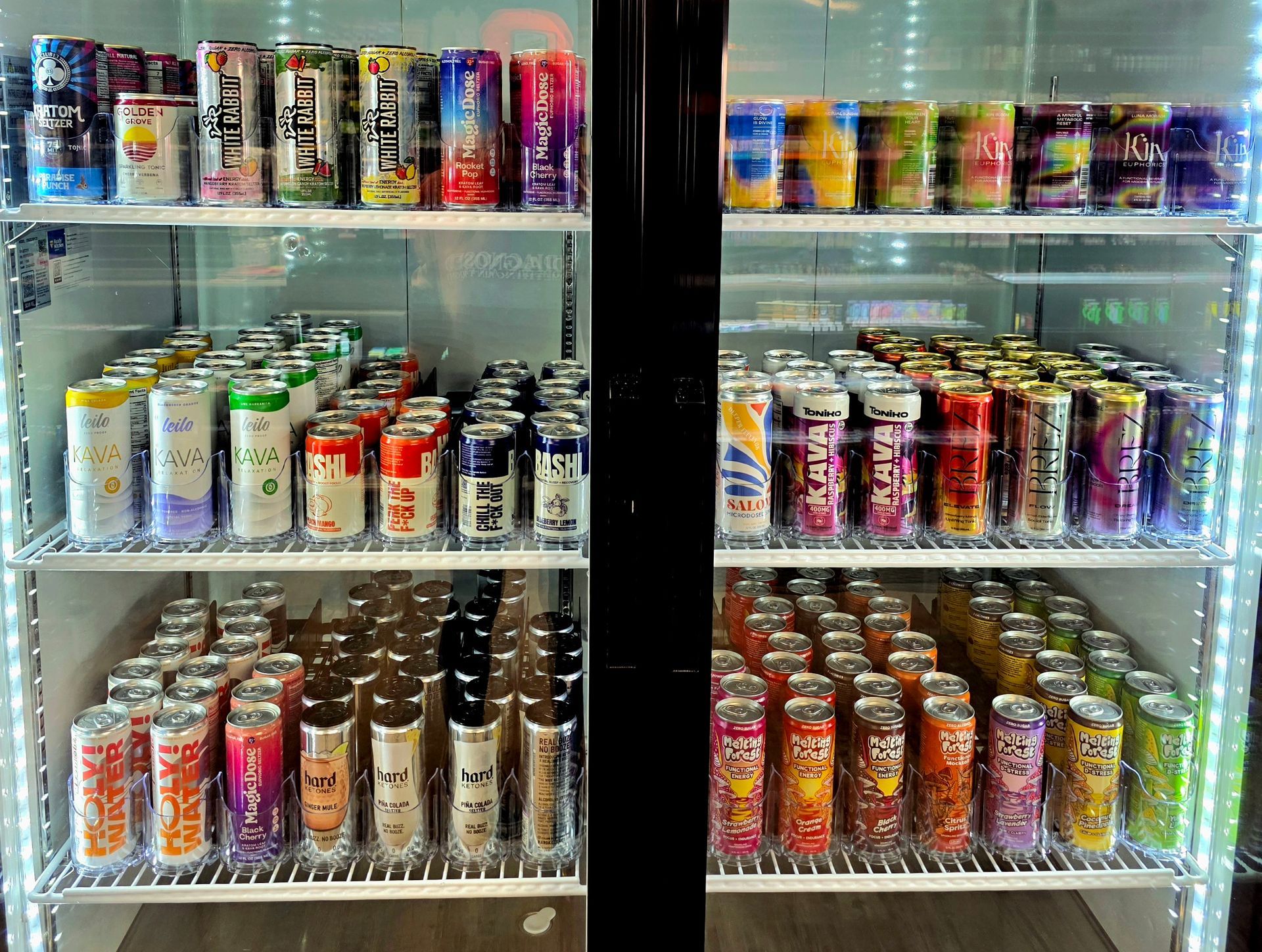 A refrigerated display case filled with rows of colorful canned energy drinks and beverages on three illuminated shelves.