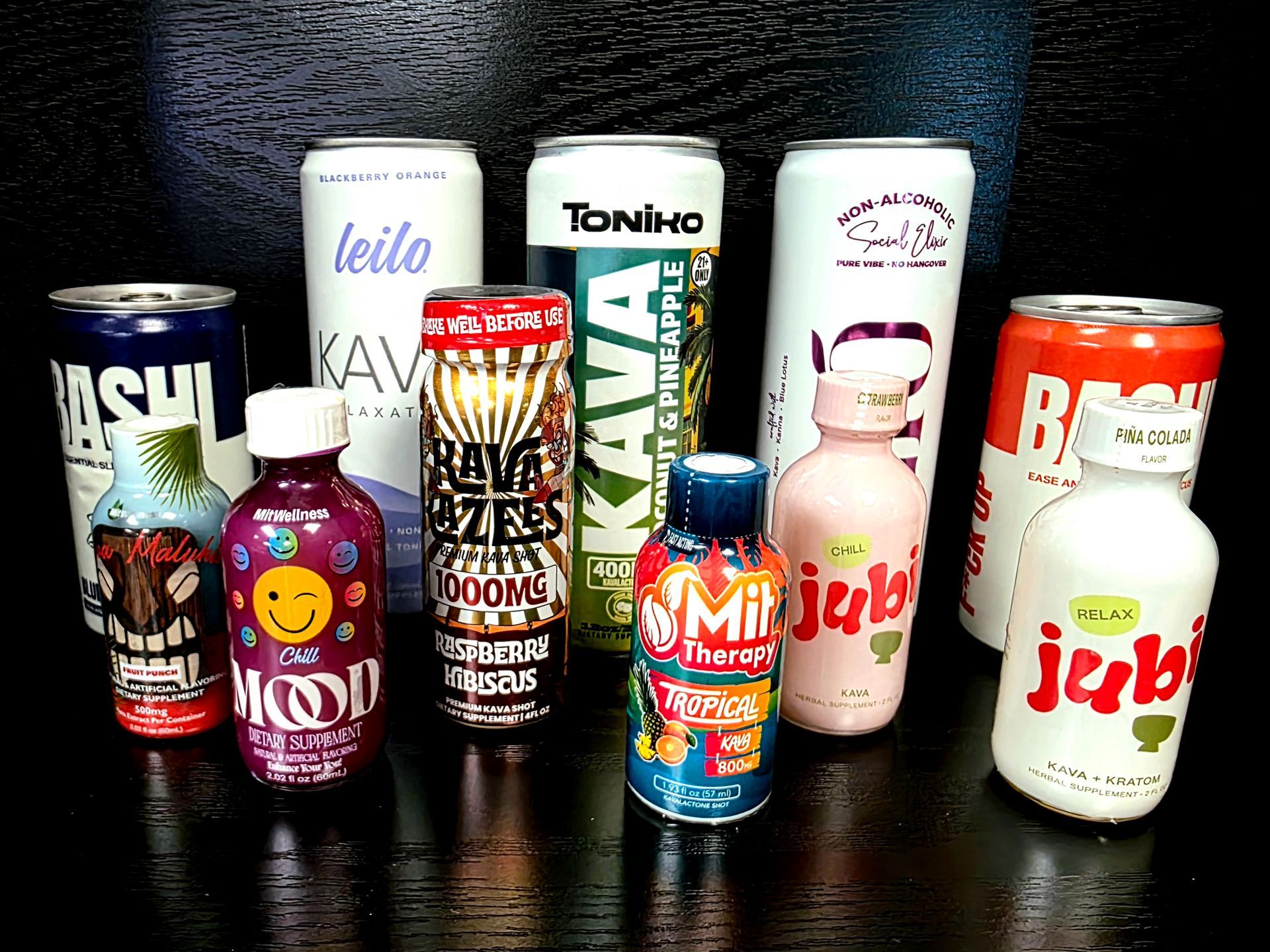 An assortment of various colorful Kava and relaxation beverage cans and small bottles arranged on a dark surface.