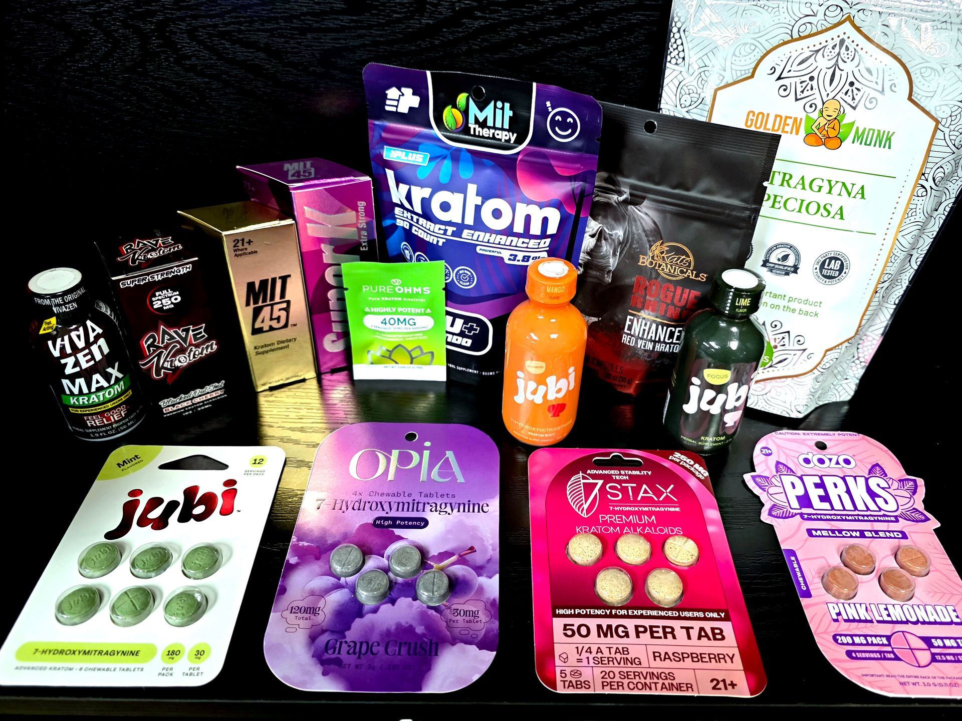 A variety of Kratom products including capsules, tablets, and liquid shots arranged on a dark surface.