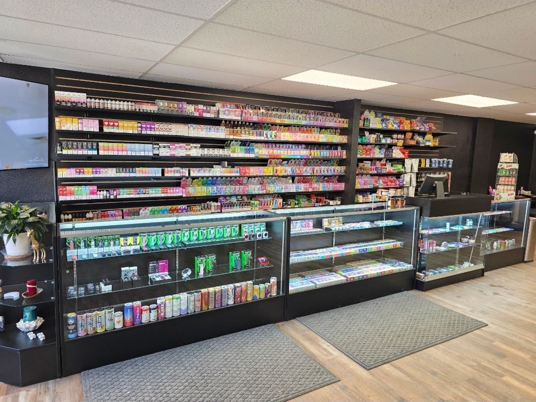 A retail store interior features long glass display cases filled with products, backed by shelves of colorful merchandise.