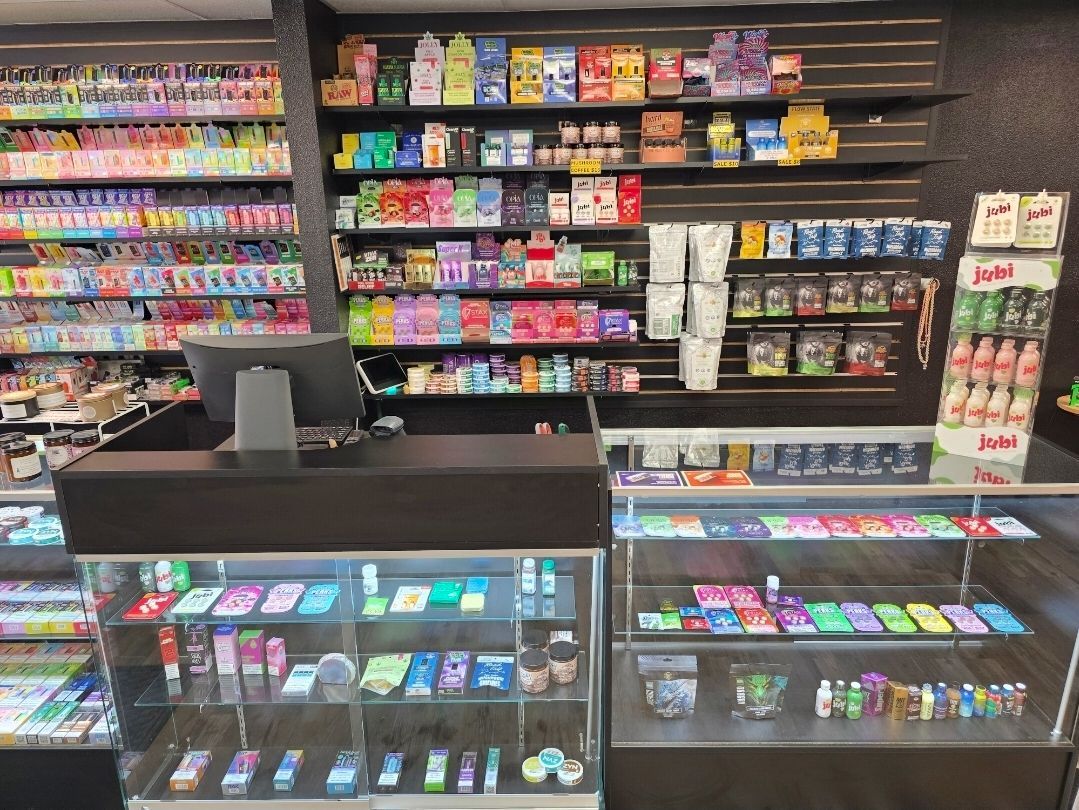 A convenience store interior with a service counter, glass display cases, and shelving units filled with various products.