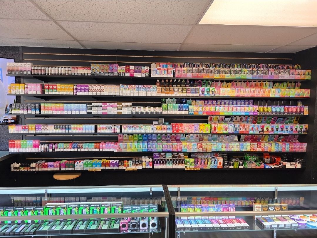 A retail store wall display filled with rows of various colorful disposable vape products and accessories.