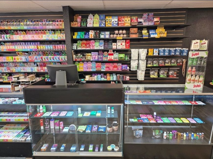 A retail shop interior featuring shelves stocked with various colorful products and a glass display counter.