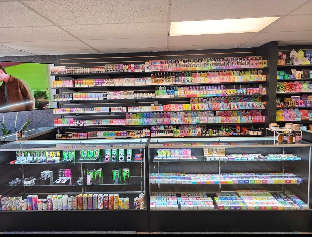 A retail counter with glass display cases filled with numerous colorful disposable vape products and accessories.