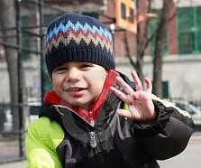 Um menino usando um chapéu e uma jaqueta está acenando para a câmera.