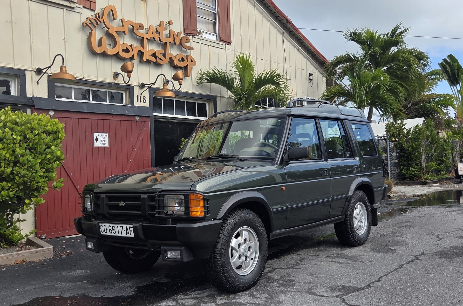 Green Land Rover Discovery SUV parked on a cobblestone driveway, surrounded by greenery.