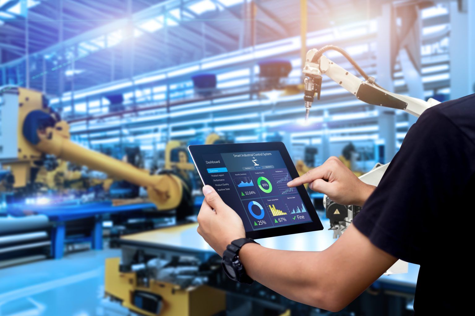 Person using a tablet to monitor industrial robots in a factory.