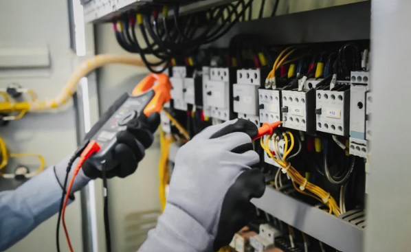 Electrician testing wiring in an electrical panel with a multimeter, wearing gloves.