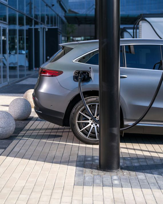 Gray electric SUV charging at a black station, next to a building with stone spheres.
