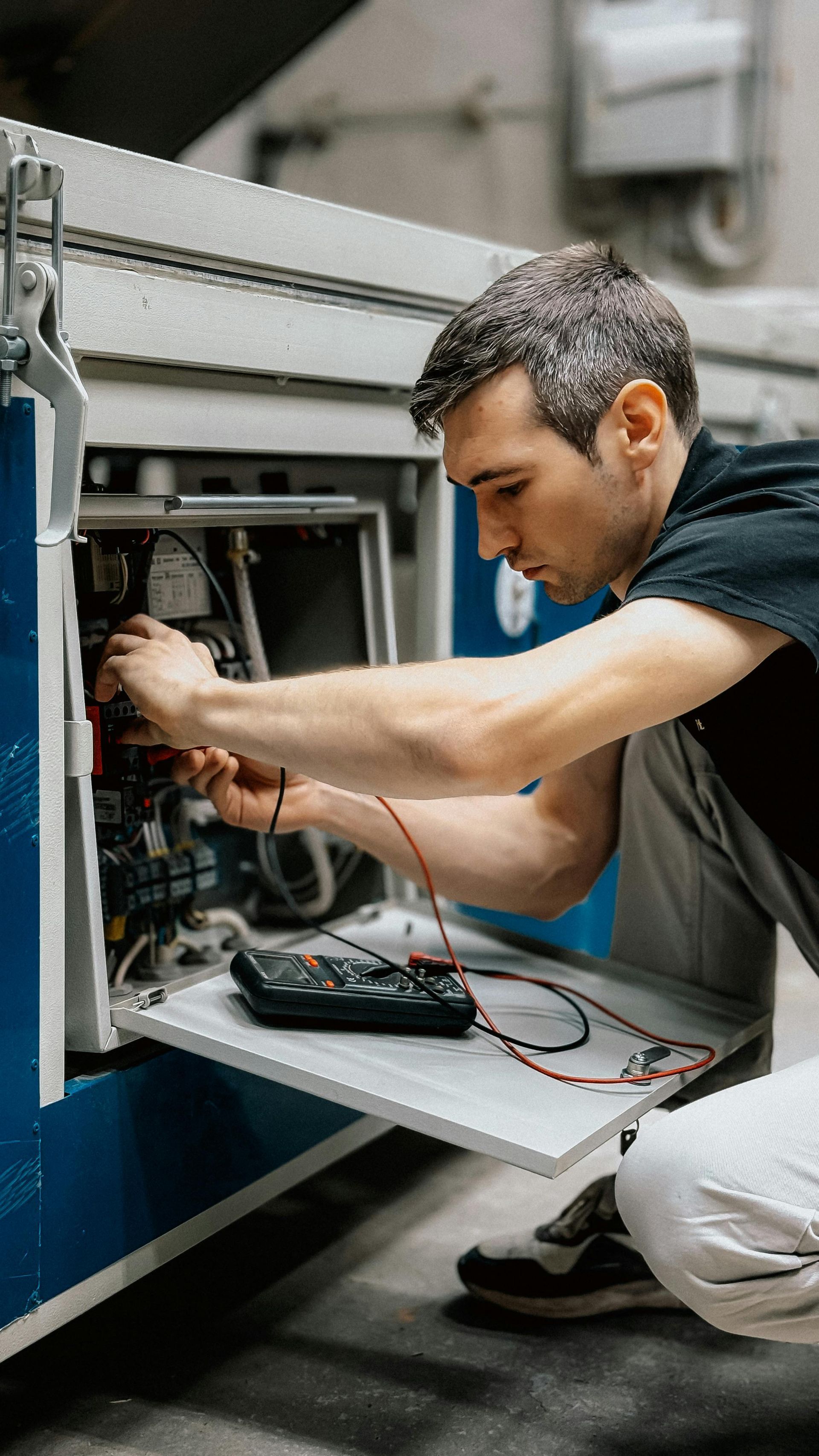 Man in black shirt, using a multimeter to repair machinery.