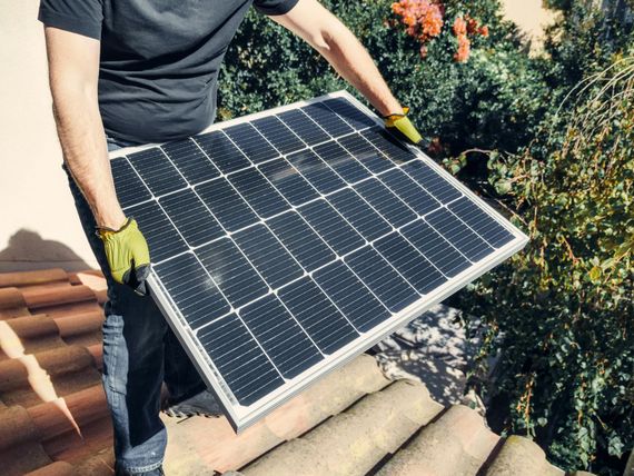 Person in gloves installing a solar panel on a tiled roof.