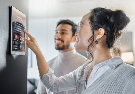 Woman interacting with a smart home control panel on a tablet, smiling, with a man looking on.