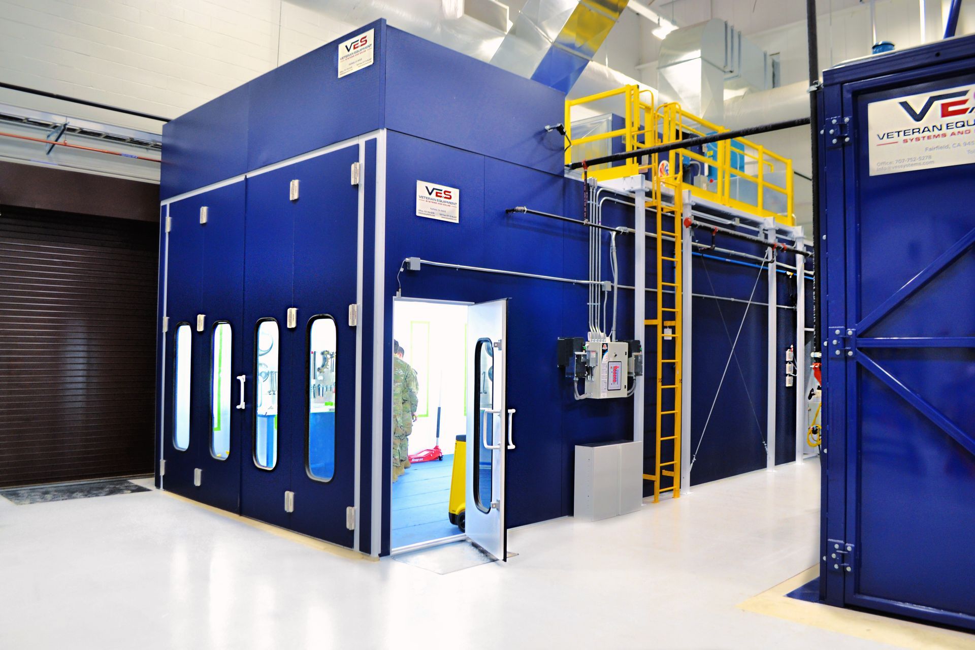 Blue industrial room with open door, vertical vents, and a yellow access platform.