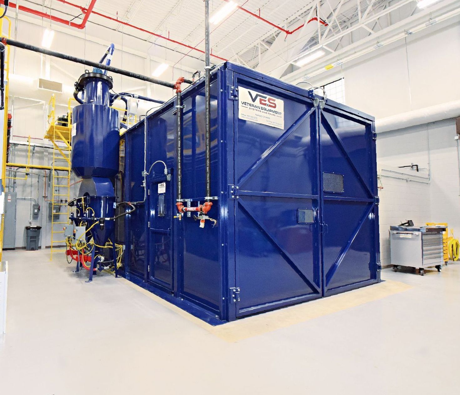 Blue industrial machine inside a brightly lit room with piping and gauges.