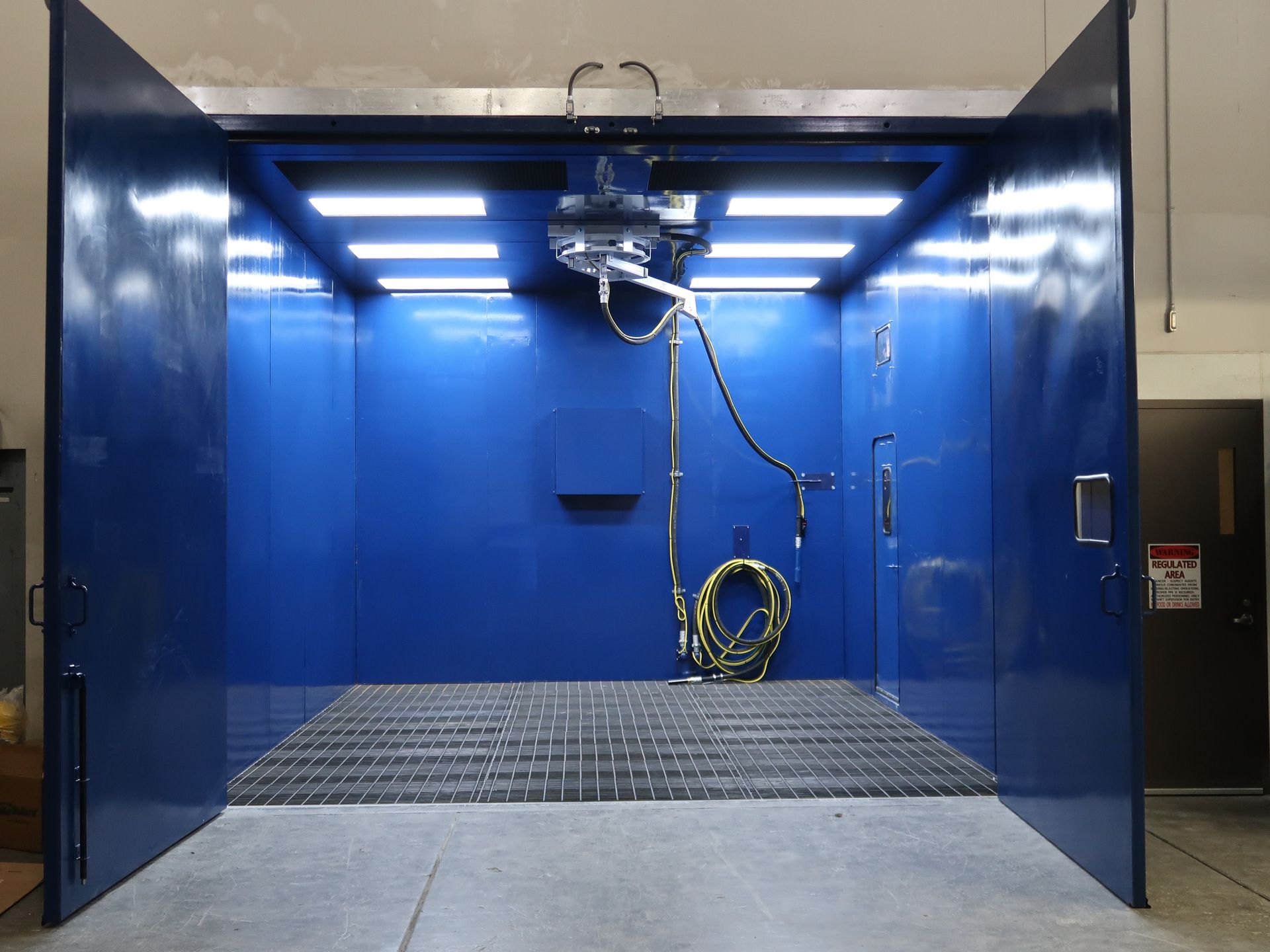 Blue paint booth with open doors, grating floor, lights, and spray equipment.