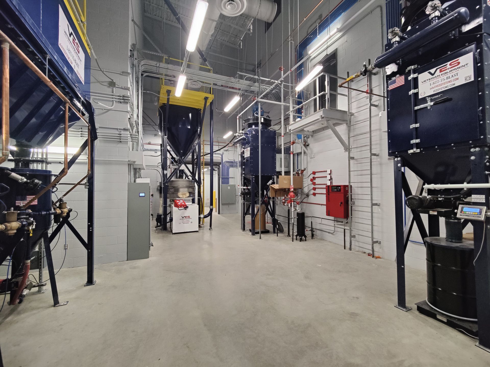 Industrial interior: machinery, pipes, and equipment in a large processing facility with concrete floors.