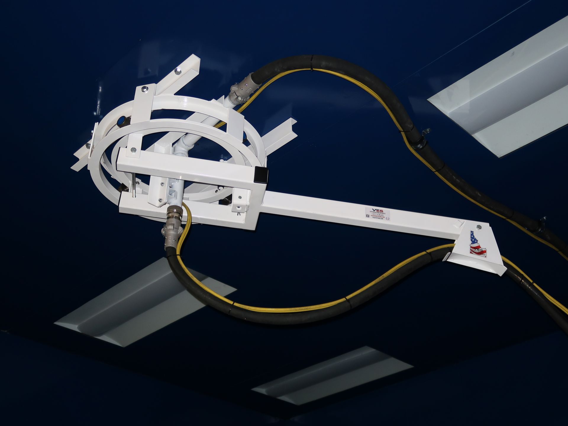 White hose reel arm attached to a dark blue ceiling, with two yellow-striped black hoses.