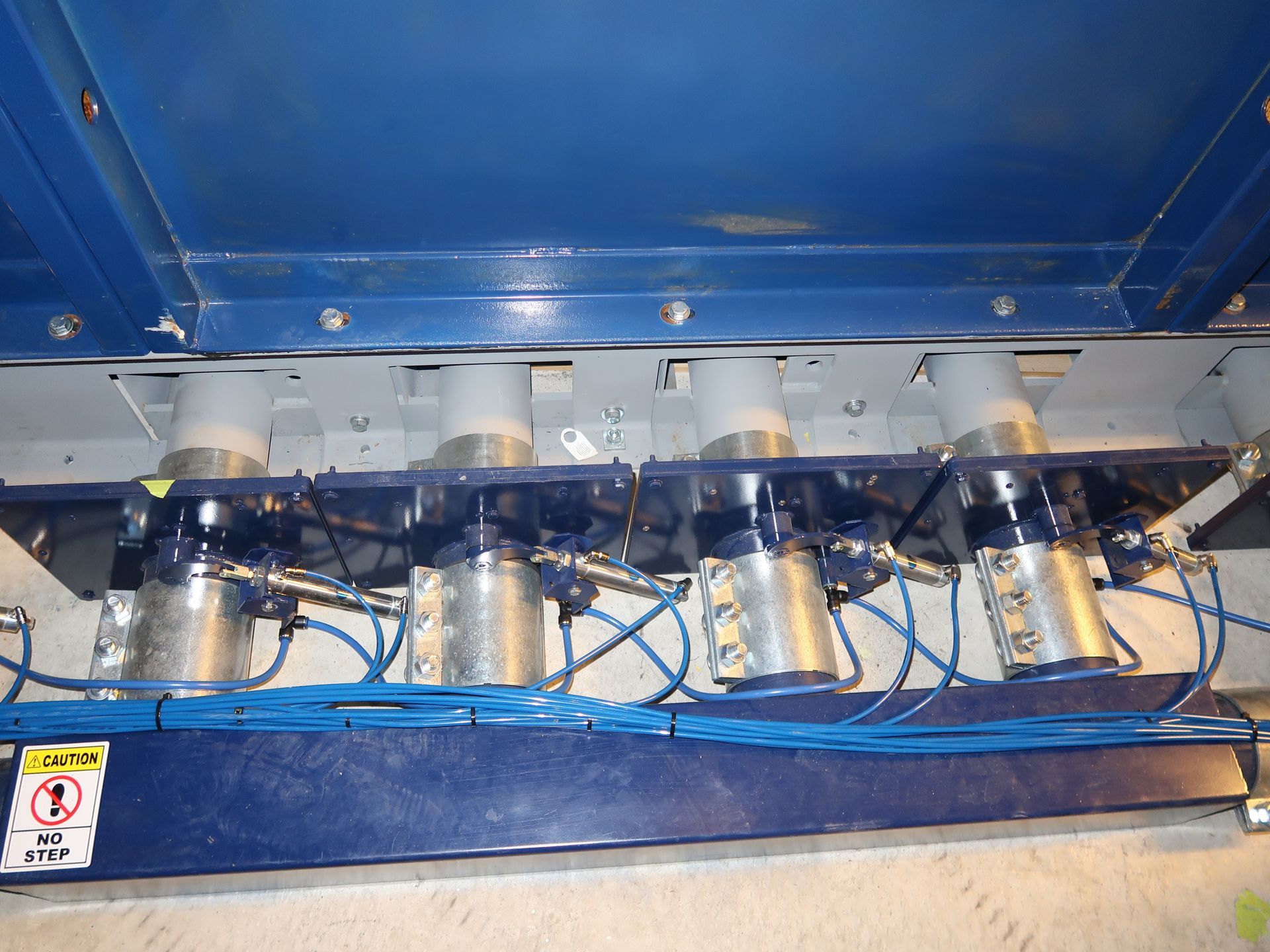Four cylindrical hydraulic devices, blue cables, mounted on a blue metal frame, likely industrial.