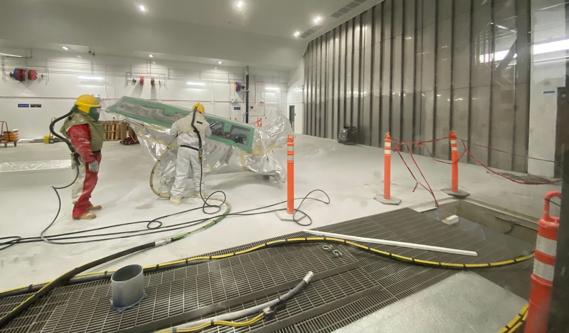 Two workers in protective suits handling a large structure in a construction zone.