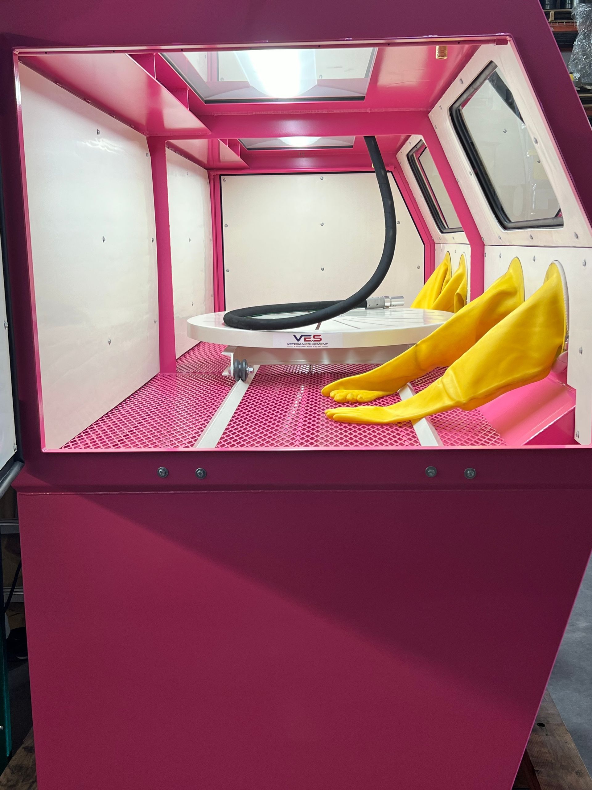 Pink sandblasting cabinet with yellow gloves, lit interior, and a clear window.