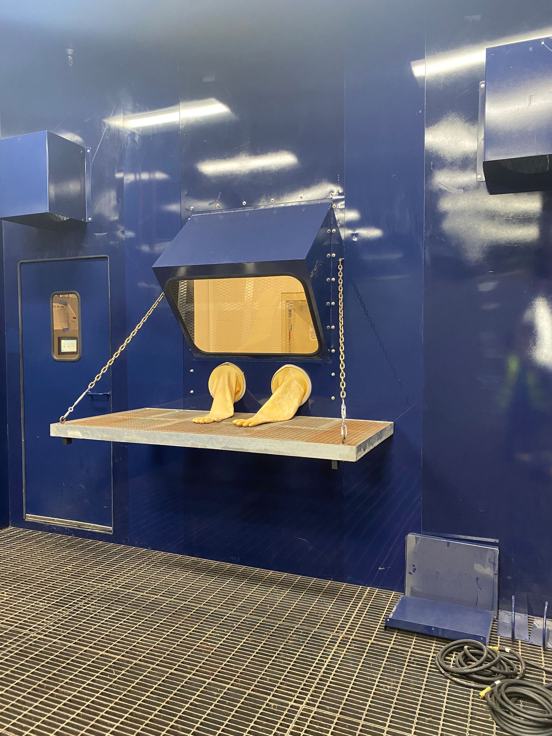 Blue containment chamber with beige gloves, a shelf, and metal chains.