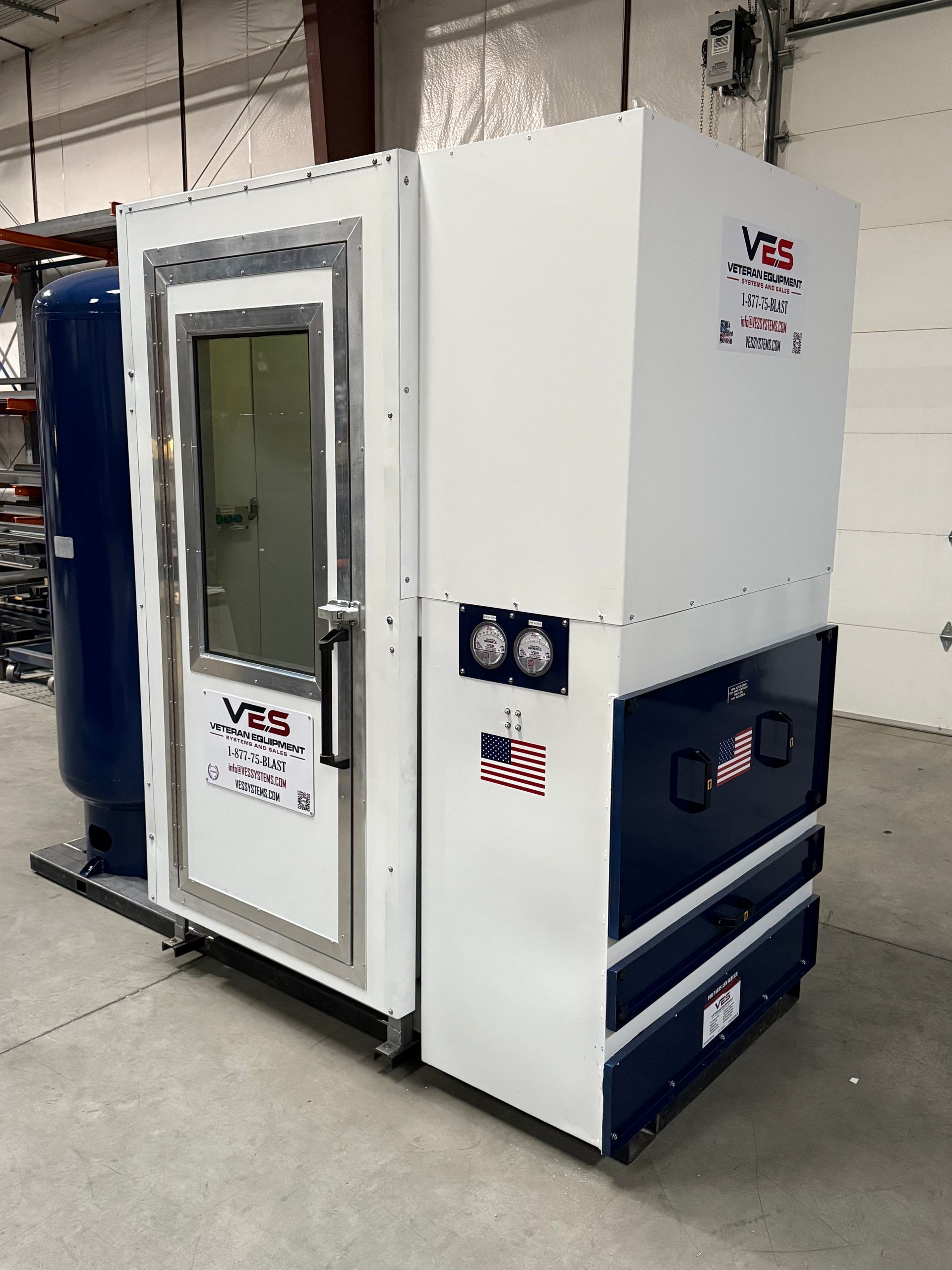 White and blue industrial unit with a door, gauges, and a flag in a warehouse.