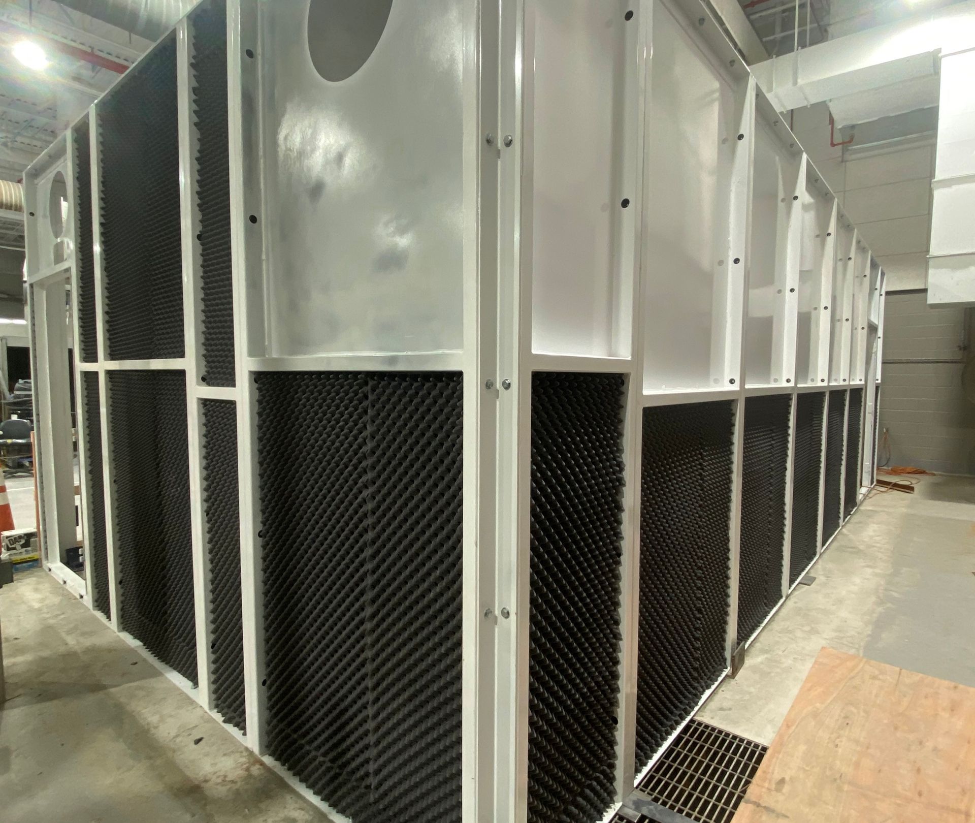 Large, white industrial structure with black sound-dampening panels installed in a building.